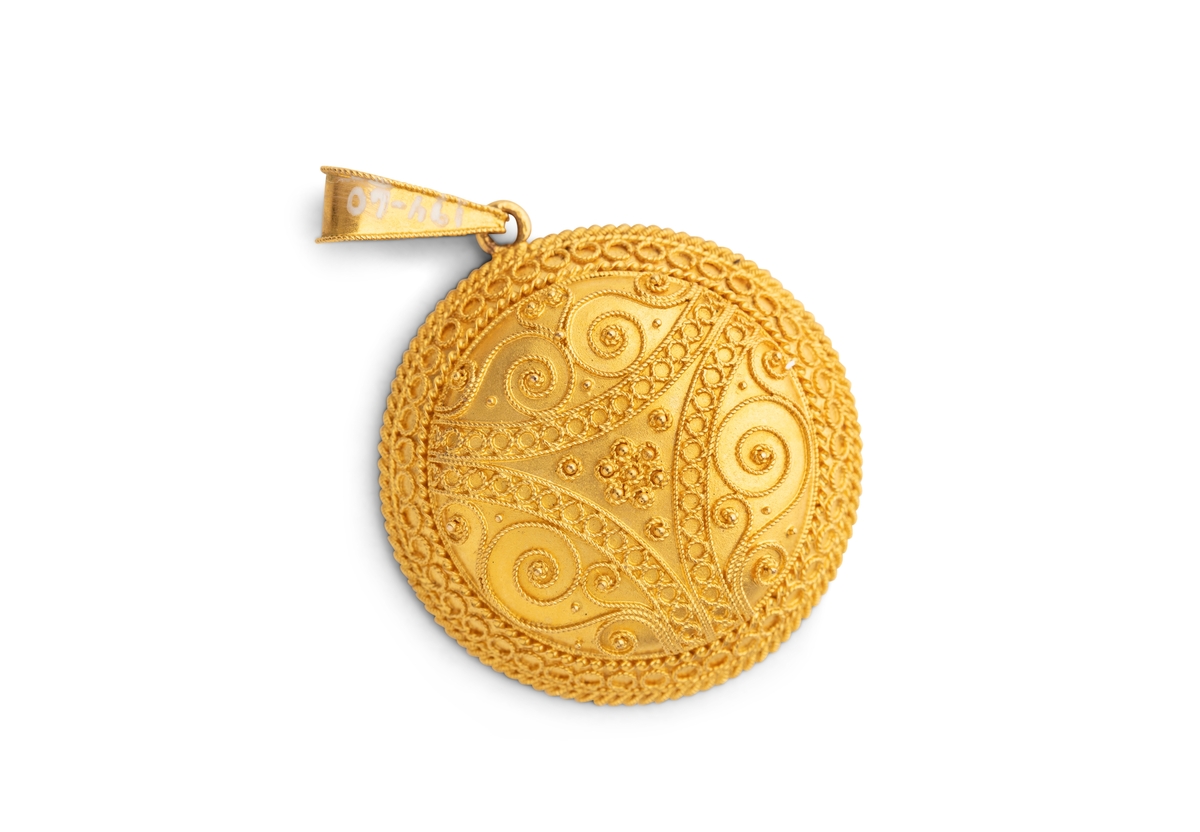 Gull sirkelformet medaljong med foto av Hans Aall som gutt. Buet med filigransarbeid, på glatt bunn, gullhempe. Ingen stempler.