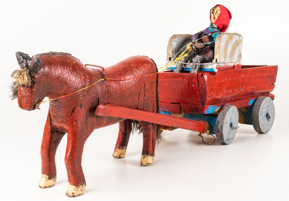 Skulptur, häst med vagn och kusk av Pehr Wassberg. Rödmålad vagn med rörliga hjul i ljusblått med sits målad i grått och guld. Vagnen dras av häst i rödbrunt med man och svans av tagel. I vagnens sits en människofigur av ståltråd och tyg. Pehr Wassberg kom från och verkade i Färila, norra Hälsingland, och räknas till de äktnaiva konstnärerna.
