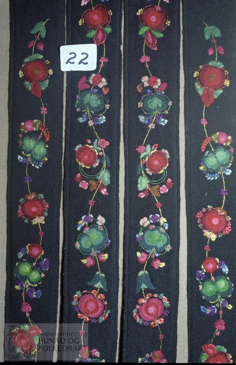 Tinn Bygdeutstilling 1985. L.: 88 cm. Br.: 4 cm. Rosesaumsranke i sterke røde sjatteringer, sterk grønne i en myk ullgarnskvalitet med effekt i diverse silkefarger.