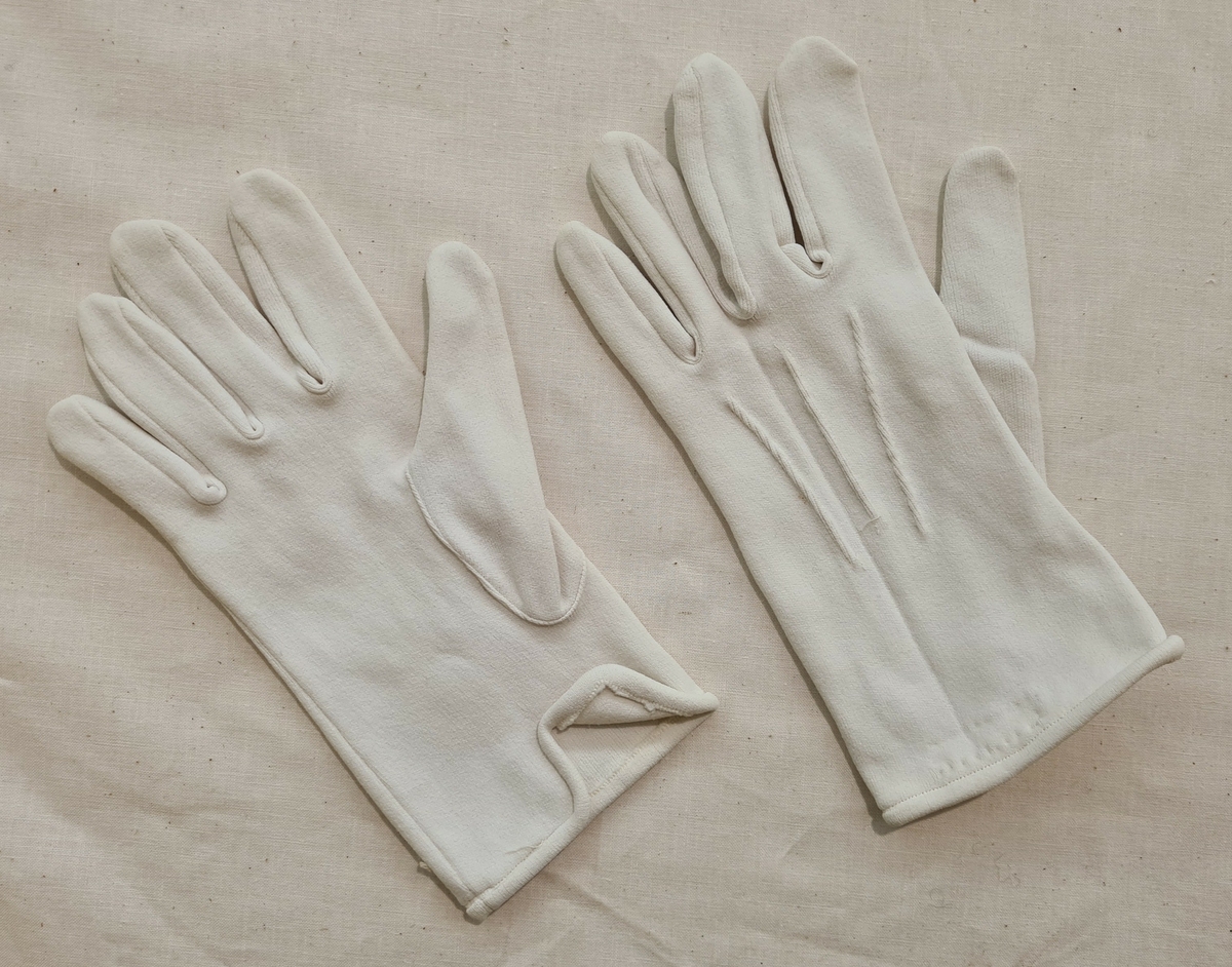 Ett par handskar av nylon till polisuniform. Handskarna har tre sydda veck på ovansidan. Vänster handske har en påsydd etikett med texten: ''100% Nylon. S-T-R-E-T-C-H Size:13/15 Made in Hong Kong.

21 272:a Höger handske.
    ''       :b Vänster handske.