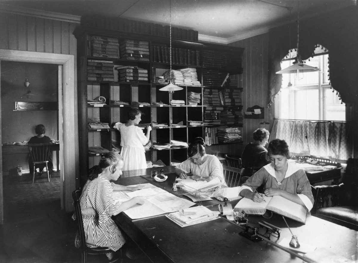Kvinner i arbeid på et kontor, skriver i protokoller og jobber med aviser.