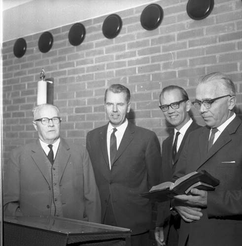 Fyra män i kostym står uppradade runt ett talarbord. Mannen till höger, Robert Svensson, håller två böcker i handen, eventuellt en bibel och en psalmbok. Olof Nilsson står intill honom.