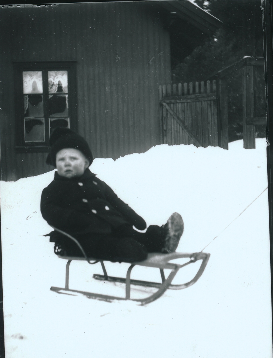 Wilhelm Fredrik Rydgren sitter på kjelke i snøen på gårdsplassen utenfor bestyrervillaen på Kistefos Træsliberi.