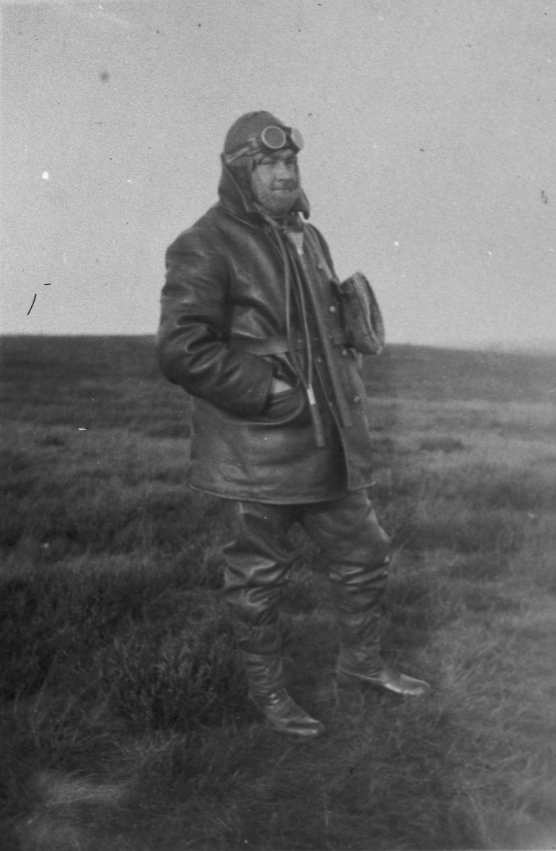 En man står i flygklädsel på ett flygfält, ca 1918-1930. Platsen är troligen Malmen.