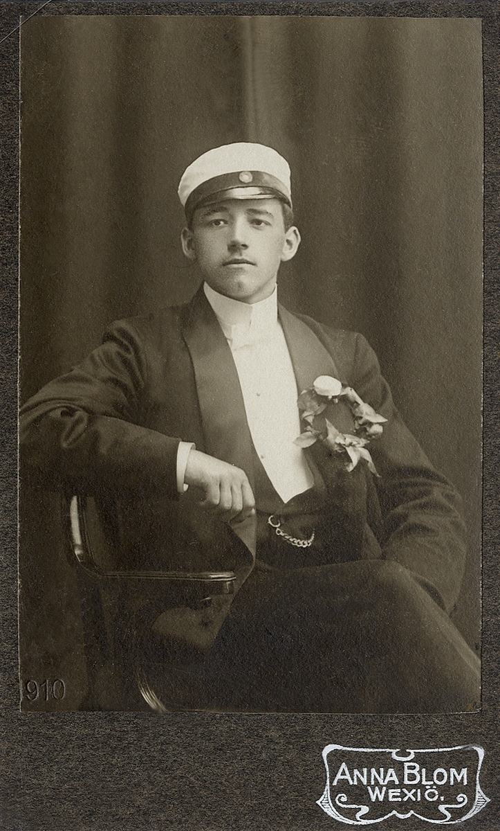 En ung man i smoking med väst, klockkedja och studentmössa.
Knäbild, halvprofil. Ateljéfoto 1910.