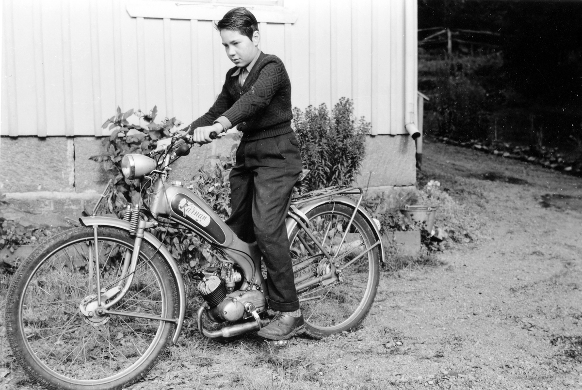 En pojke, Ulf Karlsson, sitter på en moped av märket "Kärnan", årsmodell 1954.