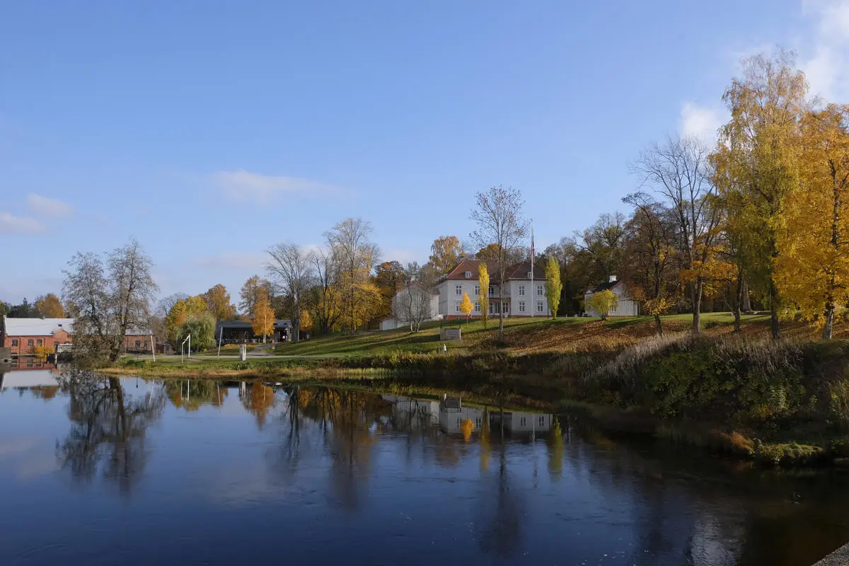 Eidsvollsbygningen i bakgrunnen, høstfarger på trærne i parken, Andelva i forgrunnen speiler bakgrunnen i vannet