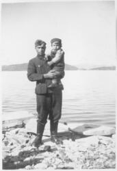 Mann i uniform med en liten gutt på armen. Fjord i bakgrunne