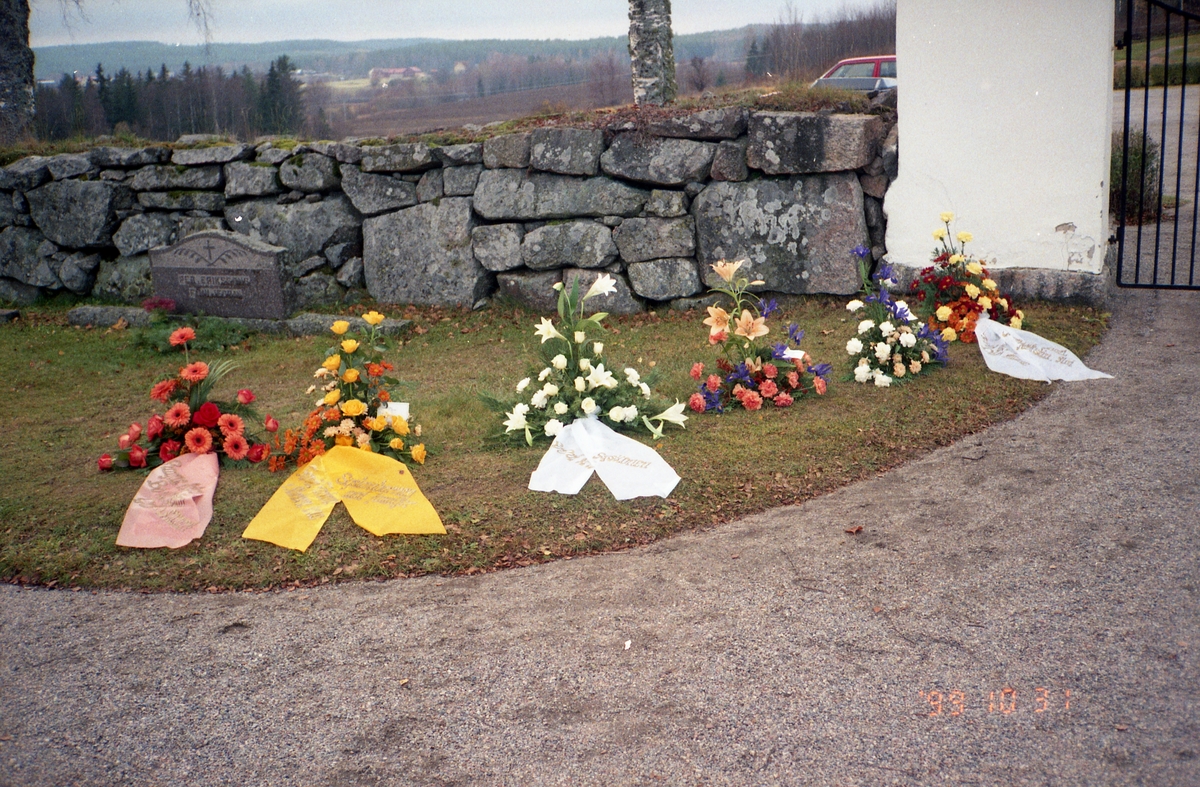 Gravbuketter ligger på rad på gräsmattan innaför gindarna till Rengsjö kyrkogård, 31 oktober 1999.