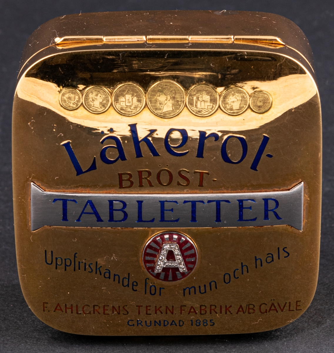 Tablettask i form av en Läkerolask, i guld med ädelstensinfattning i form av briljanter inlagda i bokstaven A på locket.
