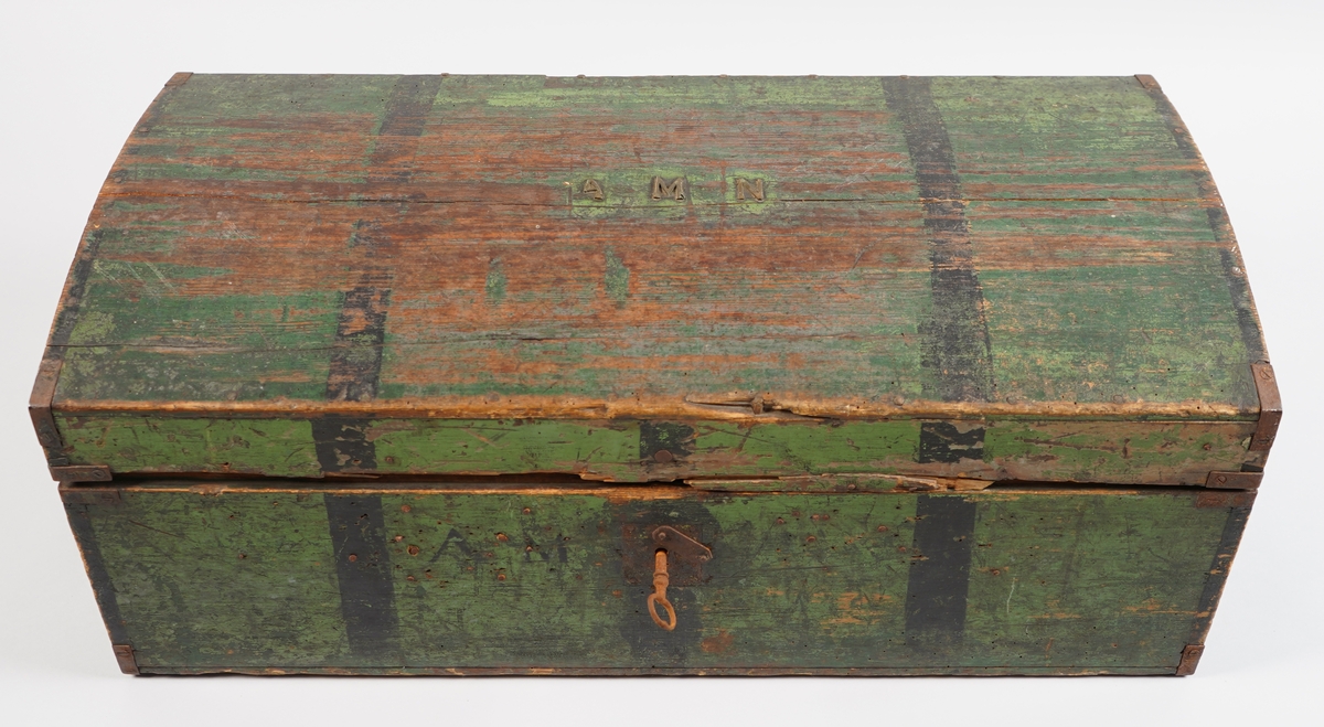 Ein grønmåla koffert i tre. Loket er forma av eit bord og er boga. Hjørna er halde saman med nokre "sinktapper" samt forsterka med metallvinkler. Kofferten har lås, og handtak i båe ender.