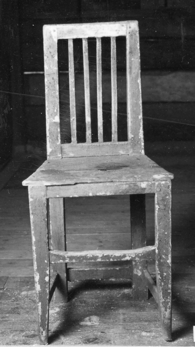 Grönmålad stol med genombruten rygg bestående av 4 vertikala spjälor. Raka 4-sidiga ben, framtill ngt avsmalnade, tvärslåar.