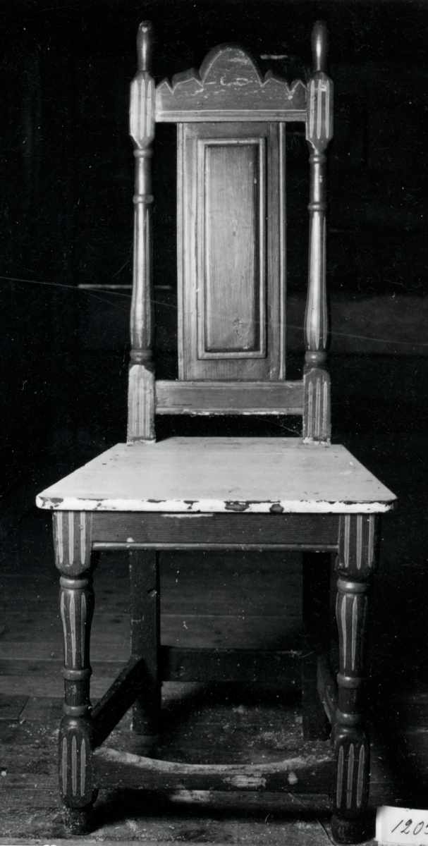Målad stol med svarvade framben och ryggstolpar, hög rygg med ryggbricka, lågt sittande tvärslå, träsits.