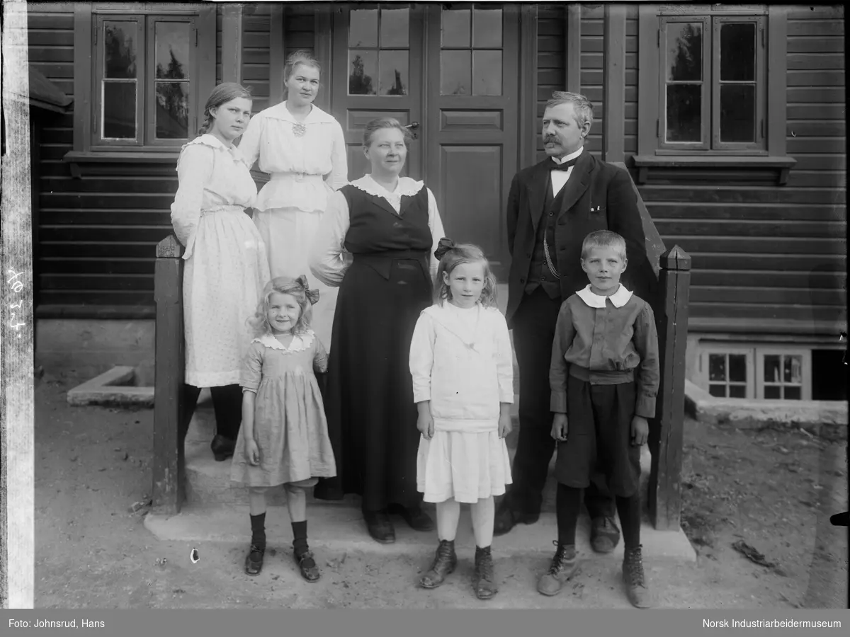 Gruppebilde av tre kvinner, to jenter, en mann, og en gutt ståendei inngangspartiet til et hus