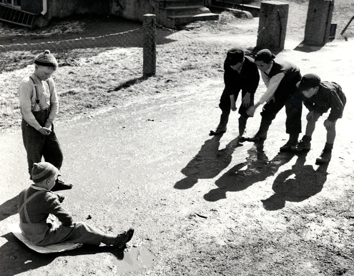 Några pojkar håller på att spela kula på en liten grusväg.