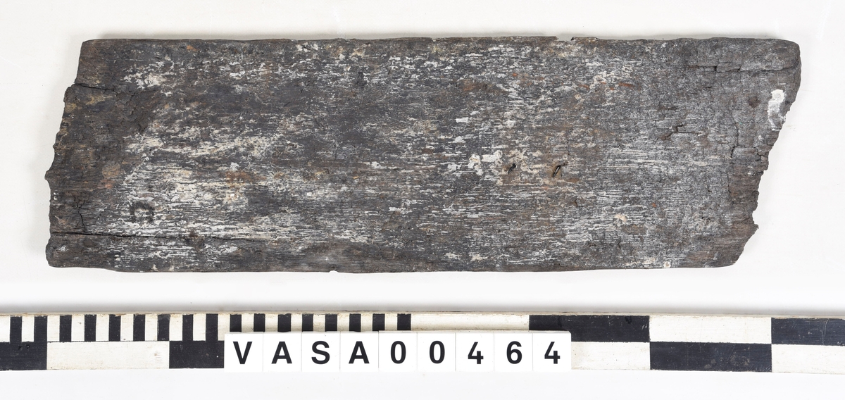 Fragment av odekorerad bräda med spår av järn i ena änden.
Mycket vittrad och flagnande. Sprickor längs båda långsidor.