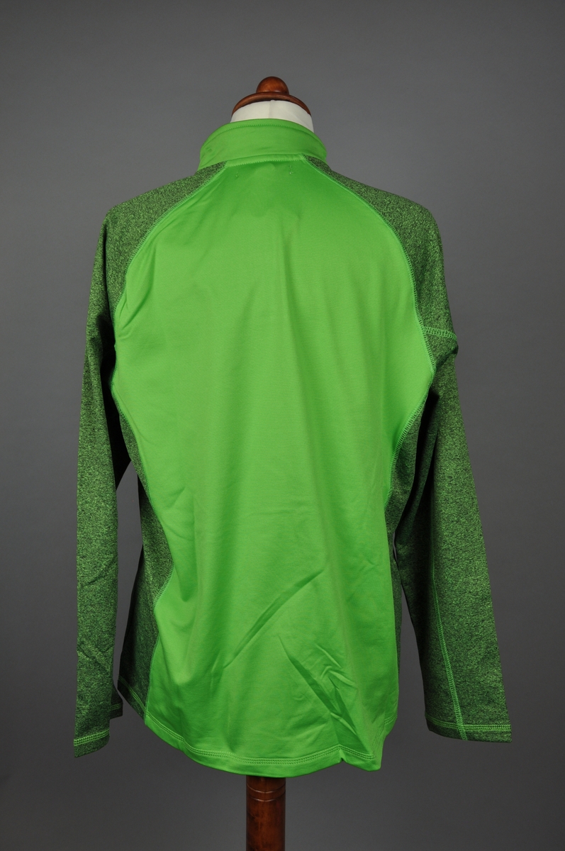 Grønn langermet genser i micropolyester med børstet innside. Glidelås ved halsåpningen. Genseren er i størrelse "Medium". Plagget har en melert mørkegrønn tone på ermer og sidene. Et brodert logomerke på fremsiden.
