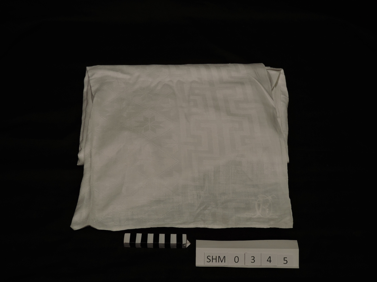 Lin, damask spisebordduk. 8-bladsrose i mønsteret. 
Monogram O.K. sydd med hvit lintråd.