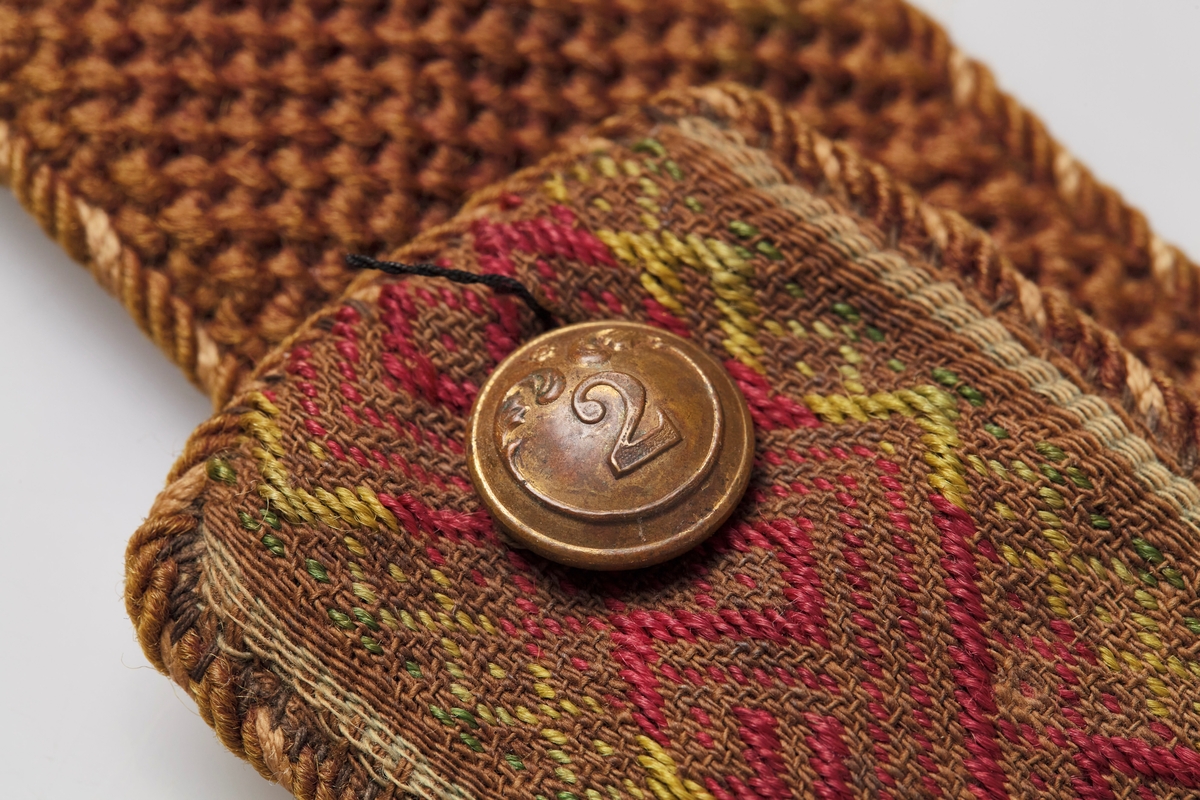 På den ene siden er det brodert "O. Rognstad 1892" med blanke perler på brun bunn. Motsatt side er dekorert med mange farger og har en knapp i hver ende.