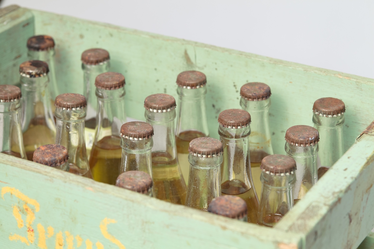 Grønn trekasse til å ha flasker i, med 20 sitronlæskedrikk flasker. Lokkene er rustet.