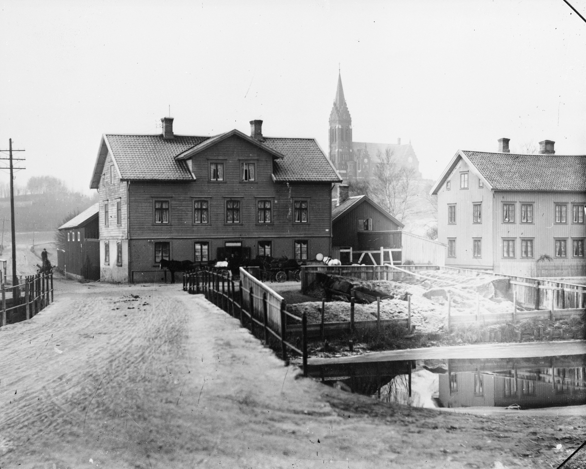 Husen på Göteborgsvägen 1-3. Till höger ses kolgården till Gustaf Pettersson på Forsåker med tillhörande hästar. Man lastar och lossar från pråmar i Mölndalsån. I bakgrunden ses Fässbergs kyrka. Bild 1996_1529 är samma foto men något mörkare.