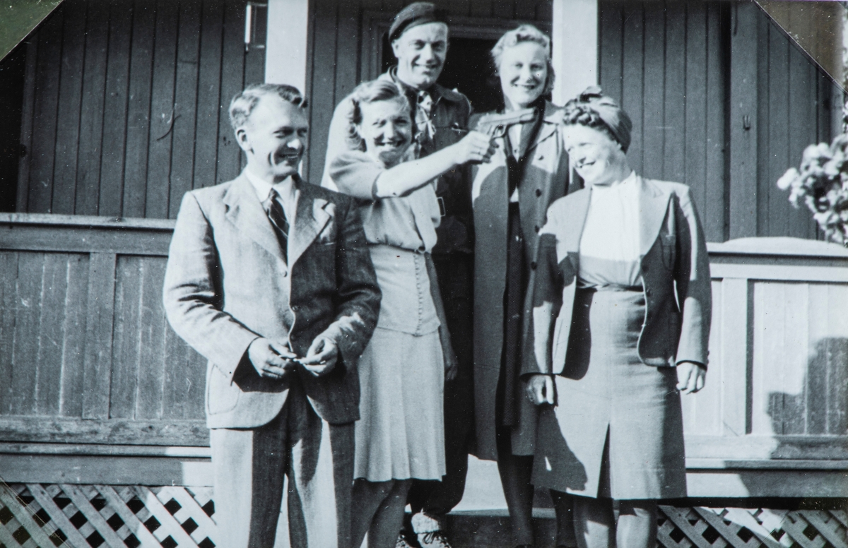 Bilder fra frigjøringsdagene i april og mai 1945. Gruppe 5 personer. Tekst under bilde i albumet er:  Sammen med Jorun og Arvid, Elna og Kåre på en liten fest på Jessnes. Dame holder en pistol i hånden.