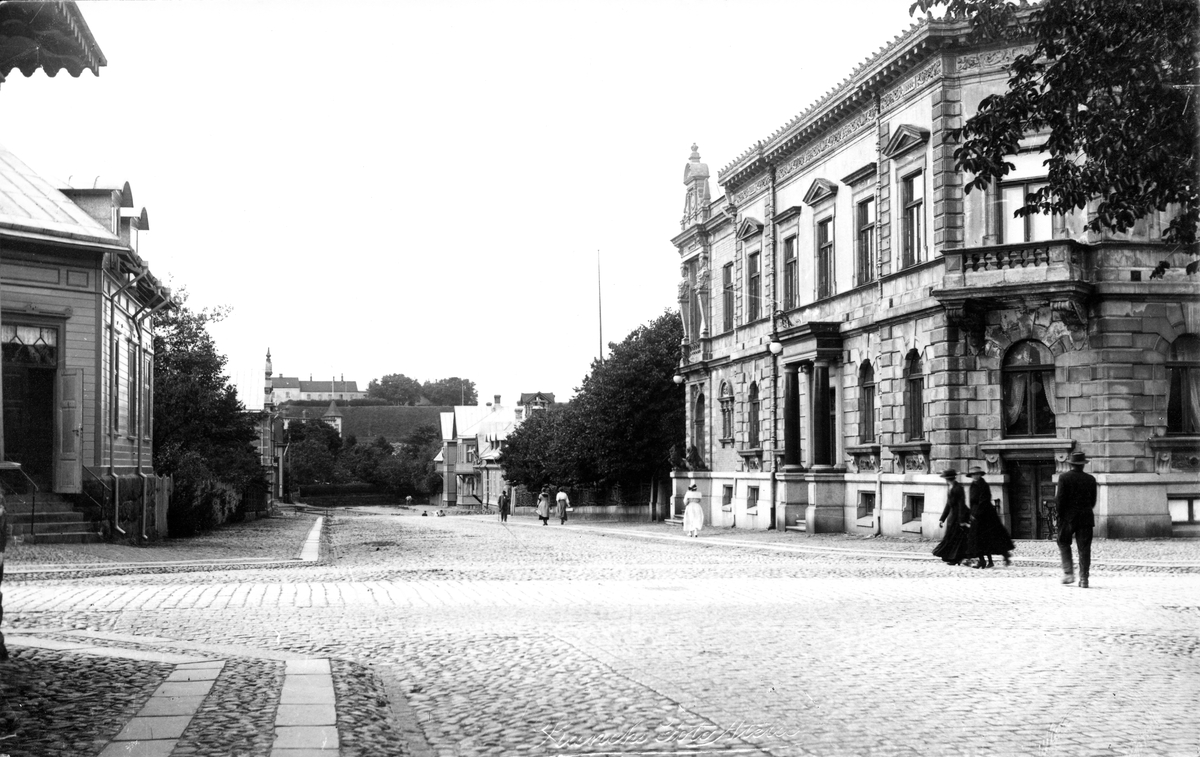 Närmast kameran till höger syns Gerlachska huset, uppfört 1891 i kvarteret Trädgården, korsningen Bäckgatan/Västra Vallgatan. I fonden av Bäckgatan ser man Societetsparken och fästningen.