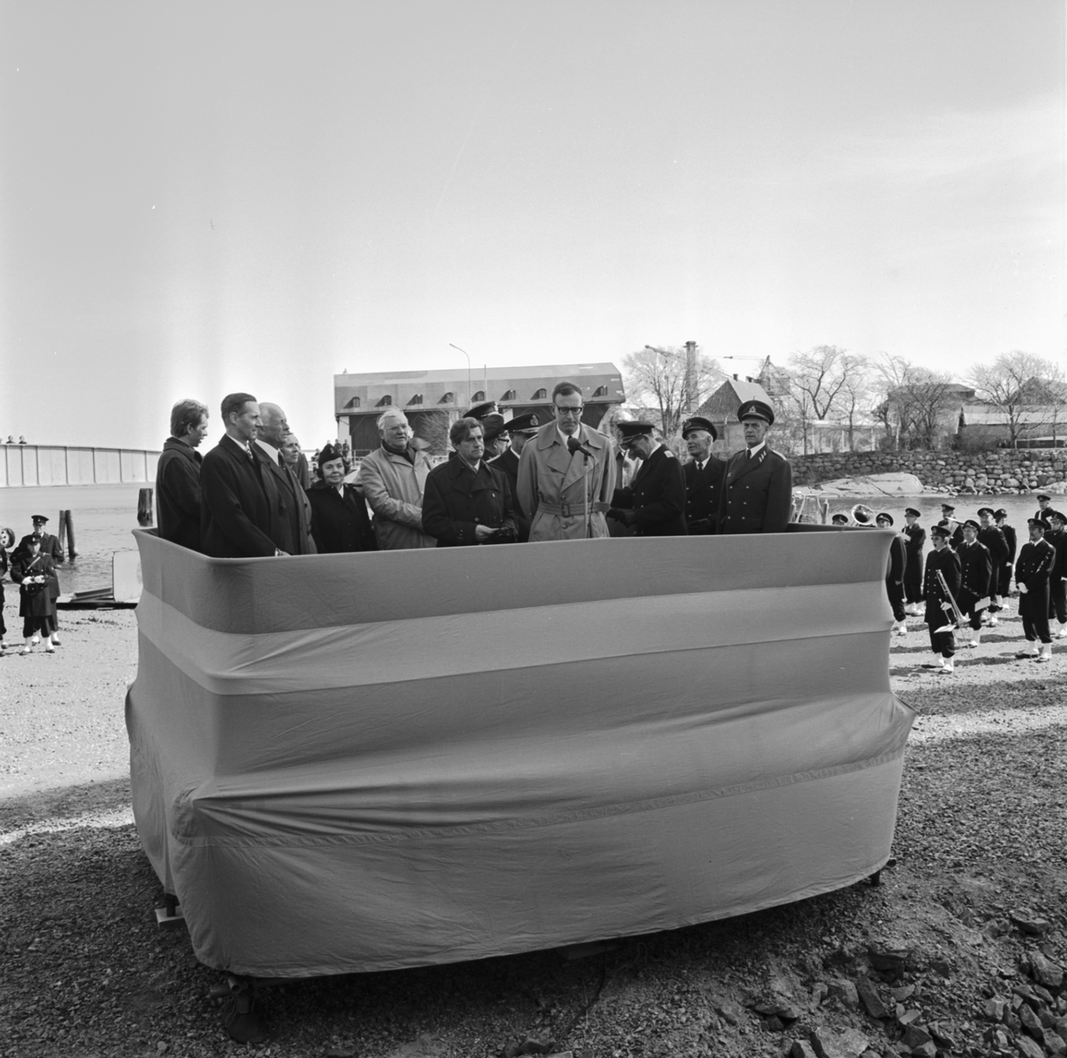 På en podium står en munter skara höga militärer och politiker som håller tal under sjösättningen av T 141. I bakgrunden syns Wasaskjulet.