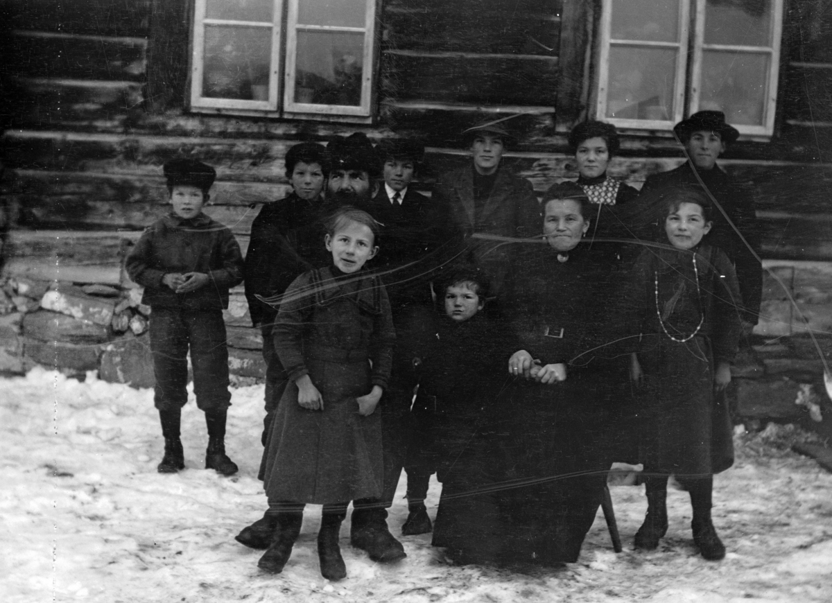 Familien Fredrik Edvard Olsen Kylling med kone og ni barn samlet foran våningshuset på garden. Barn oppført etter alder.