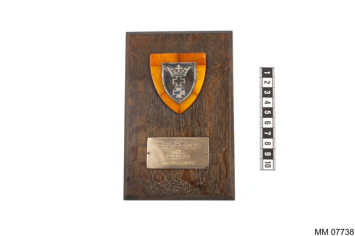 Plakett av silver på bärnsten, fastsatt till platta av trä.
Inskription på platta av nysilver: Sport-Spiele in Dantzig 11 - 16.6. 1937.