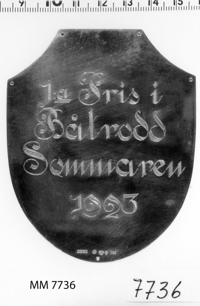 Plakett av silver utan platta.
Utgör 1:a pris i båtrodd, erövrat av Saga år 1923.
Inskription: 1a Pris i Båtrodd Sommaren 1923.