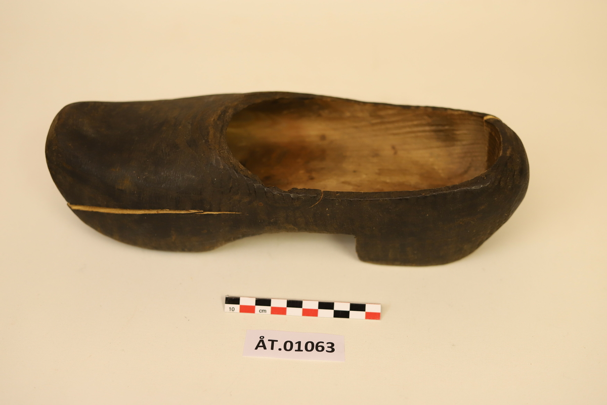 Ein mørkebrunbeisa, høgre tresko. Skoen er sprukken framme på vestre sida og bak på hælen. Sprikkene går inn mot senter av stokken. Senter er midt i skoen på lengda. Høgreist sko, mogleg heimelaga.