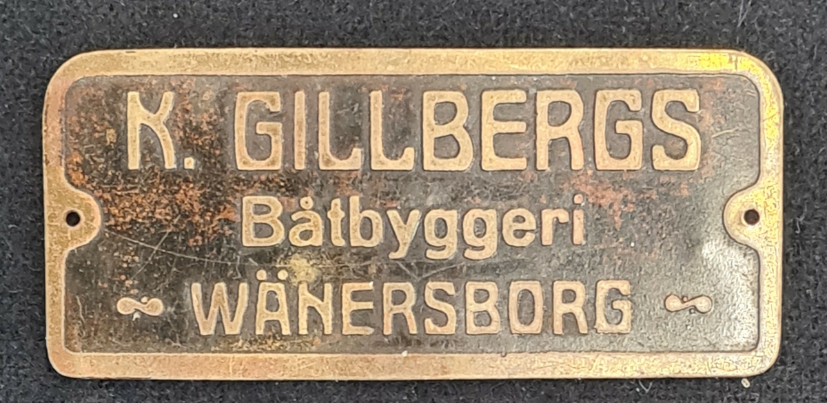 Emblem i metall. På emblemet står: K. Gillbergs Båtbyggeri Wänersborg