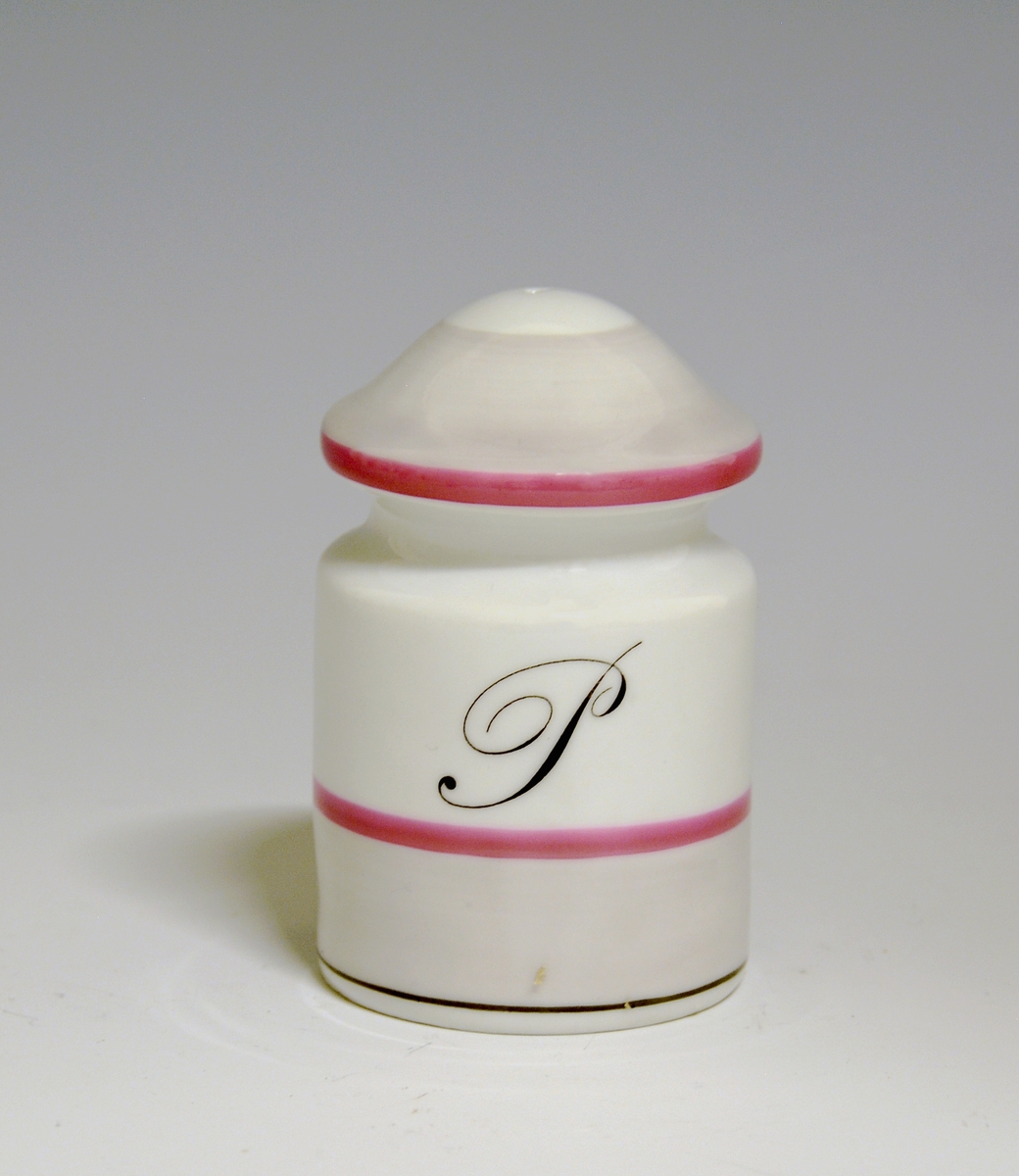 Saltdrysse av porselen. Hvit glasur. Sylindrisk form med inntrapping i øvre del. med rosa striper og grått bånd.
Modell: Eystein