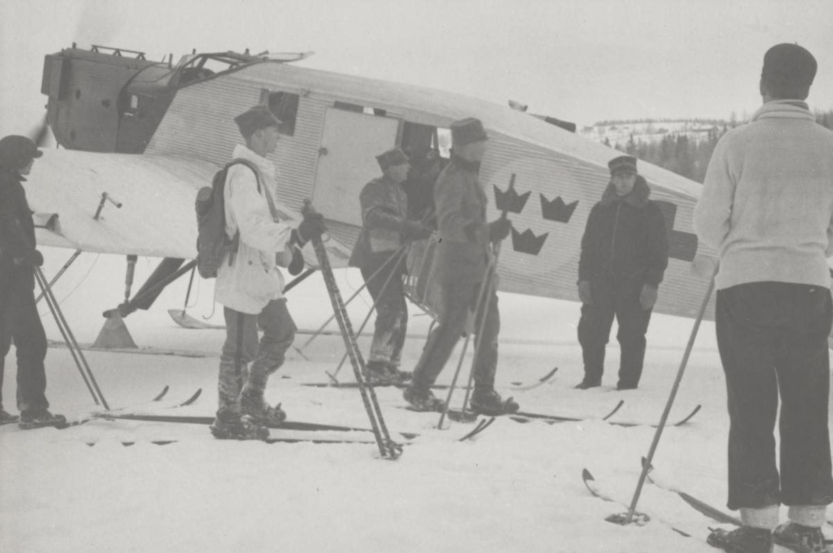 Militärer på skidor står vid ambulansflygplan Trp 2, Junkers W 34, vintertid. Flygare vid planet.