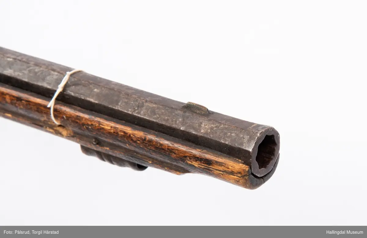 Gevær med eldre militær flintlås. Privat våpen med riflet løp. Mulig satt sammen tidlig 1800-tall.
Utskjæringer i treet bak lås. Mangler ladestokk. Ornament under lås og på kolbekappe.