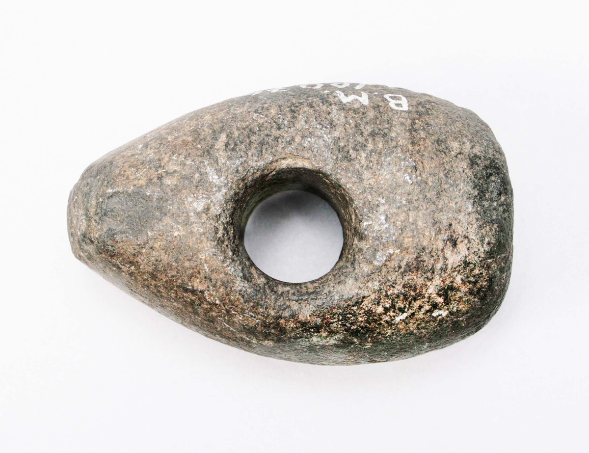 Skafthålsyxa av mörk sten. Liten, tjocknackad yxa med hål, 26 mm diam på mitten.