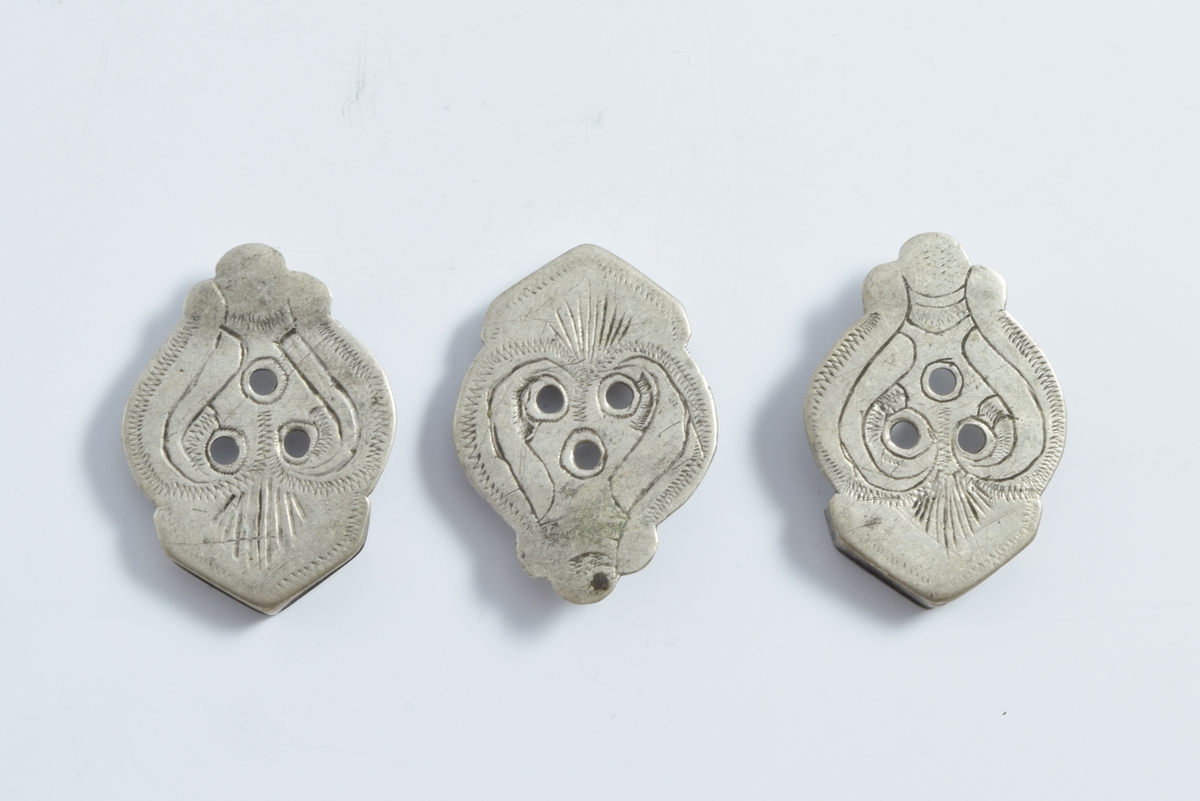 Hjertelignende figur med 3 tunger ved spissen og med gavllignende bekroning, flaten har 3 huller samt graverte ornamenter.