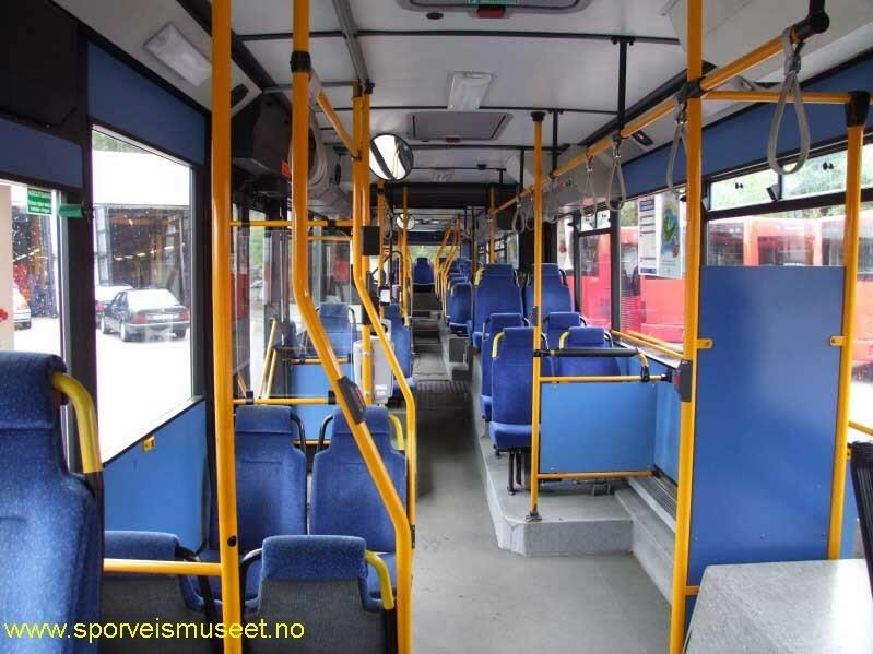 Rød leddbuss med blått parti langs langsiden. Det er tre inngangspartier med dobbeltdører. På innsiden er bussen installert med blå seter og lys gråe overflater. 
