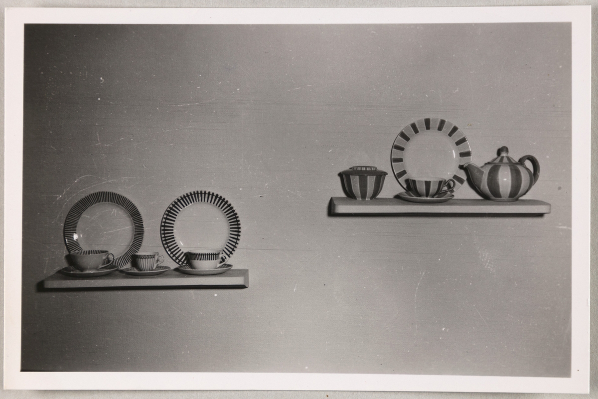 Hyller med serviser fra Stavangerflint A/S. Avbildede objekter viser tallerkener, kopper, skål med lokk og ei tekanne.