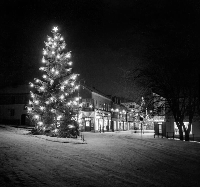 Svart-hvitt foto av stor julegran med tente lys og stjerne i toppen, ved Triangelparken i Hamar sentrum.