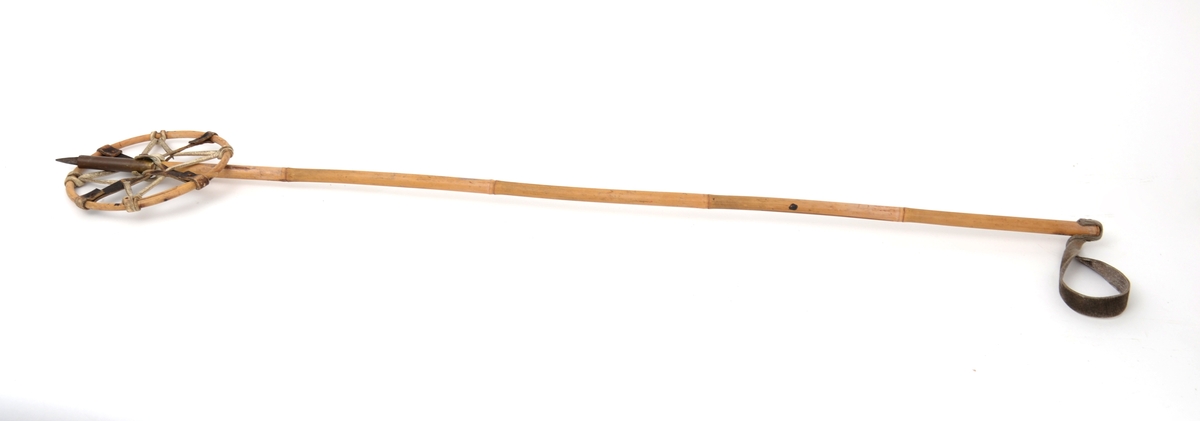 Skistav med lærhåndtak øverst og trinse av bambus med lærremmer på kryss og tvers, mellom trinsen og staven. Nederst på staven er det stanset inn et messingrør på 10 cm. og neders er det en pigg på 3,2 cm.