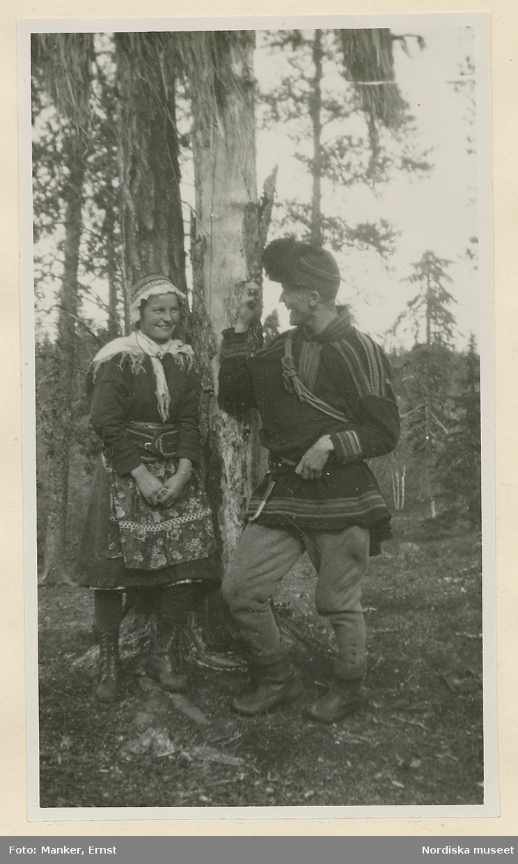 Brita Sevä, 17 år, och ingenjör Rantio står vid ett träd i Tuolpukka, Jukkasjärvi socken, och samtalar. Båda är iklädda samisk dräkt.