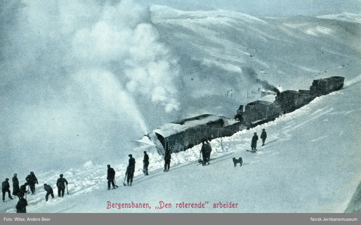 Roterende snøplog skjøvet av tre damplokomotiver med en gruppe ryddemannskaper i forgrunnen