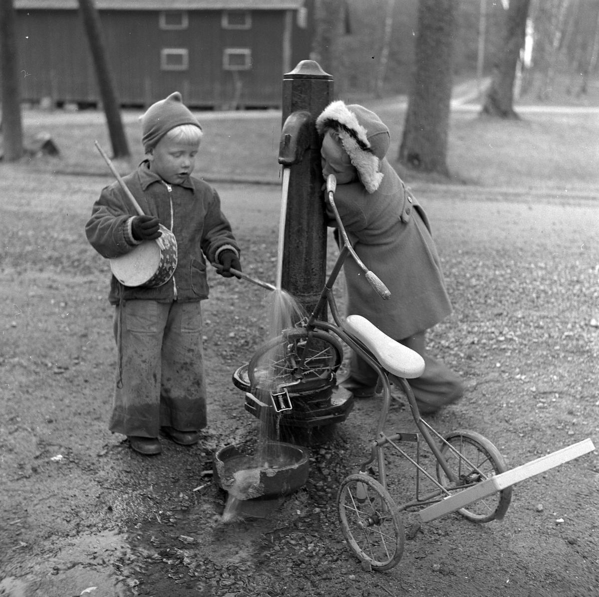 Två barn tvättar en trehjuling vid pumpen nere vid Nolhaga slott, maj 1950