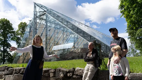 A female guide in Medieval dres is giving a guided tour to a family outside the glass cathedral.