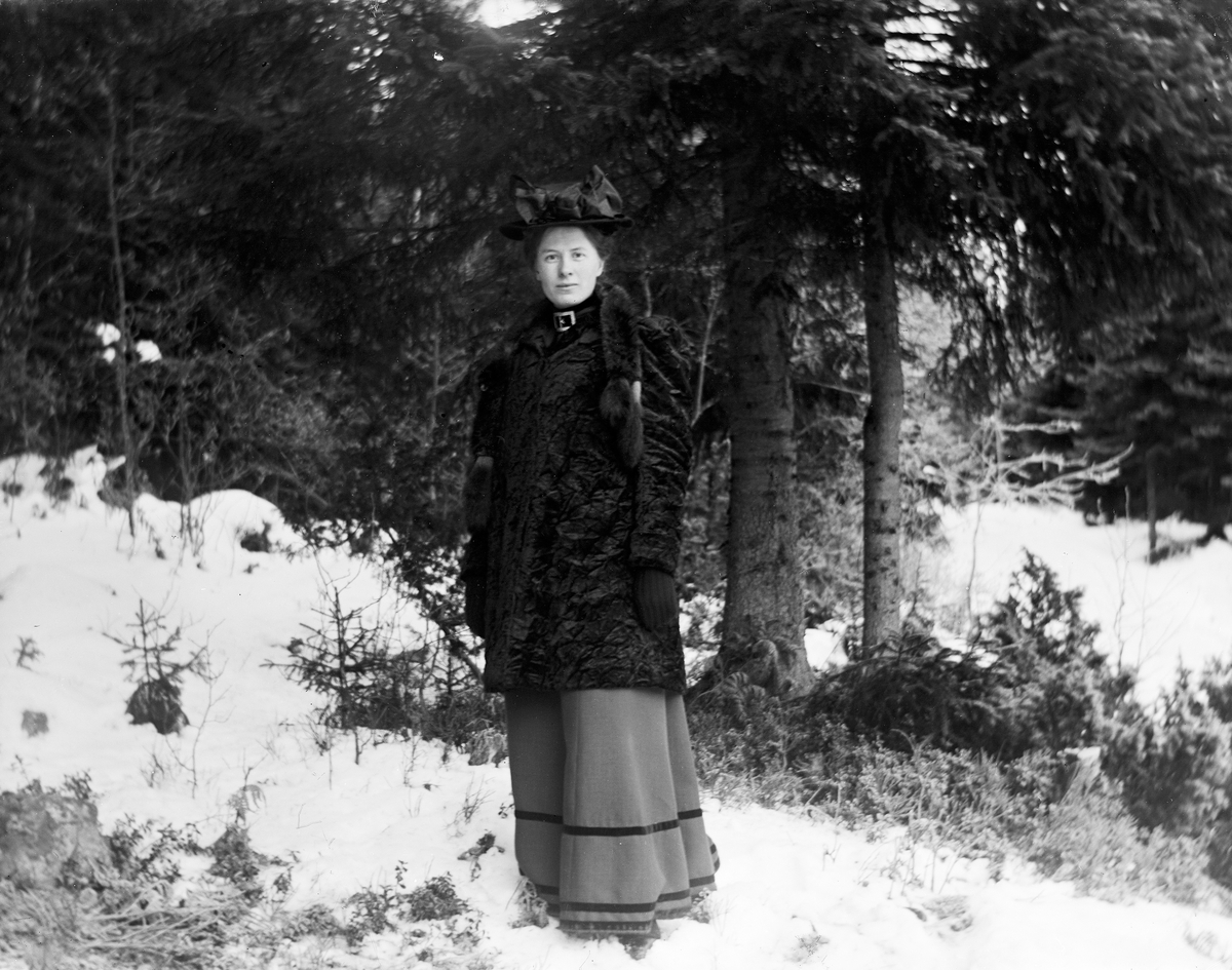 En kvinne står ute i skogen på vinterstid. 
