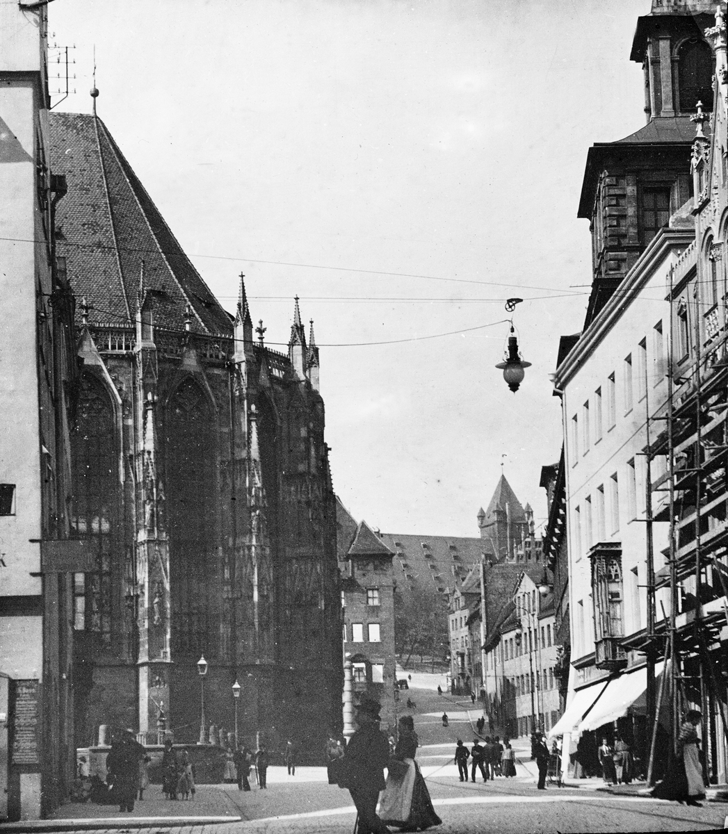 Skioptikonbild med motiv av gata vid Sankt Sebalduskirche i Nürnberg.
Bilden har förvarats i kartong märkt: Nürnberg 1901. VIII.. Text på bild: "Au Hauptmarkt"