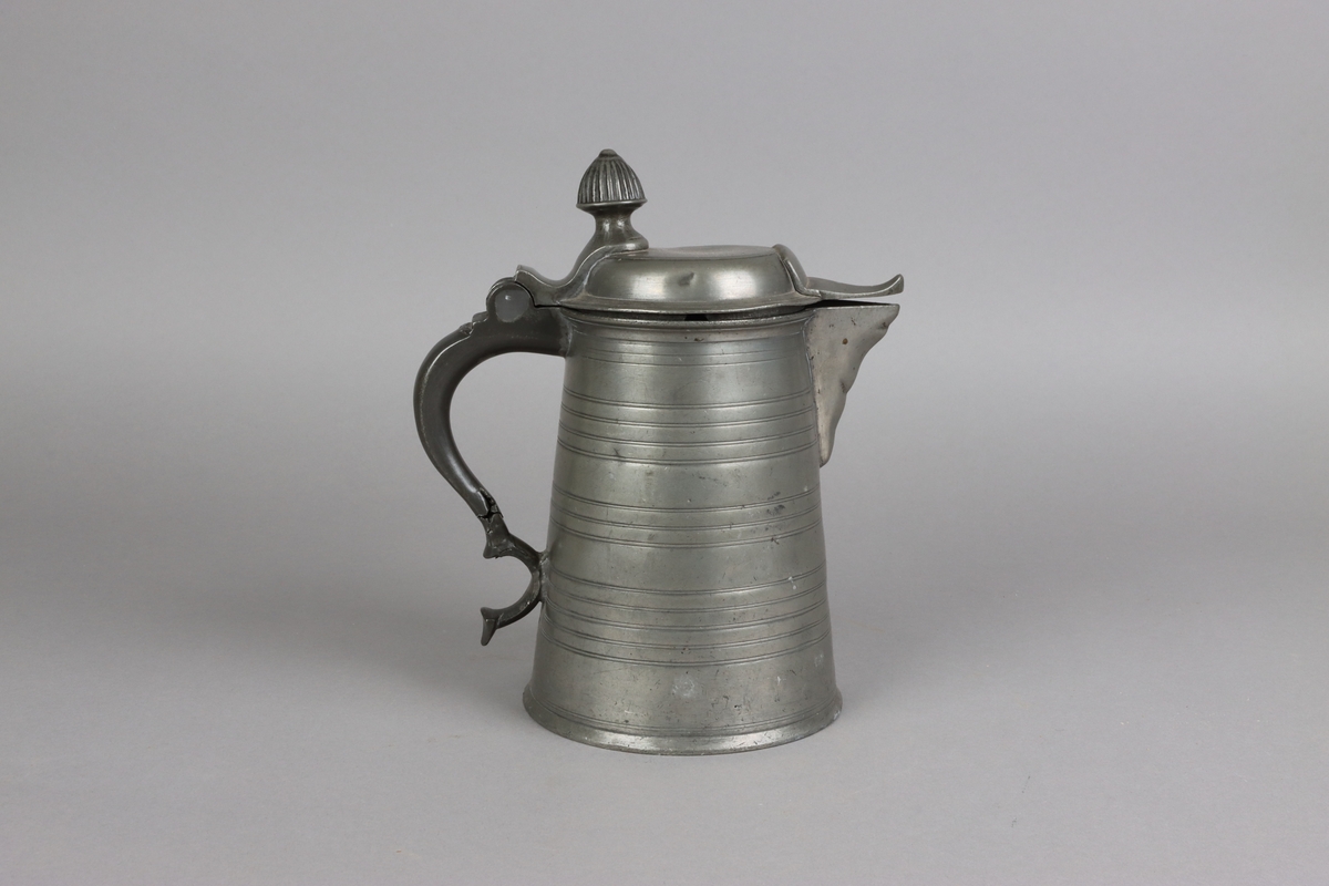 Jug and cover, all in pewter, with conical body  and a loop handle. On the cover knob in the form of a pine cone. On the body sections of horizontal borders. Five hallmarks inside the jug.
