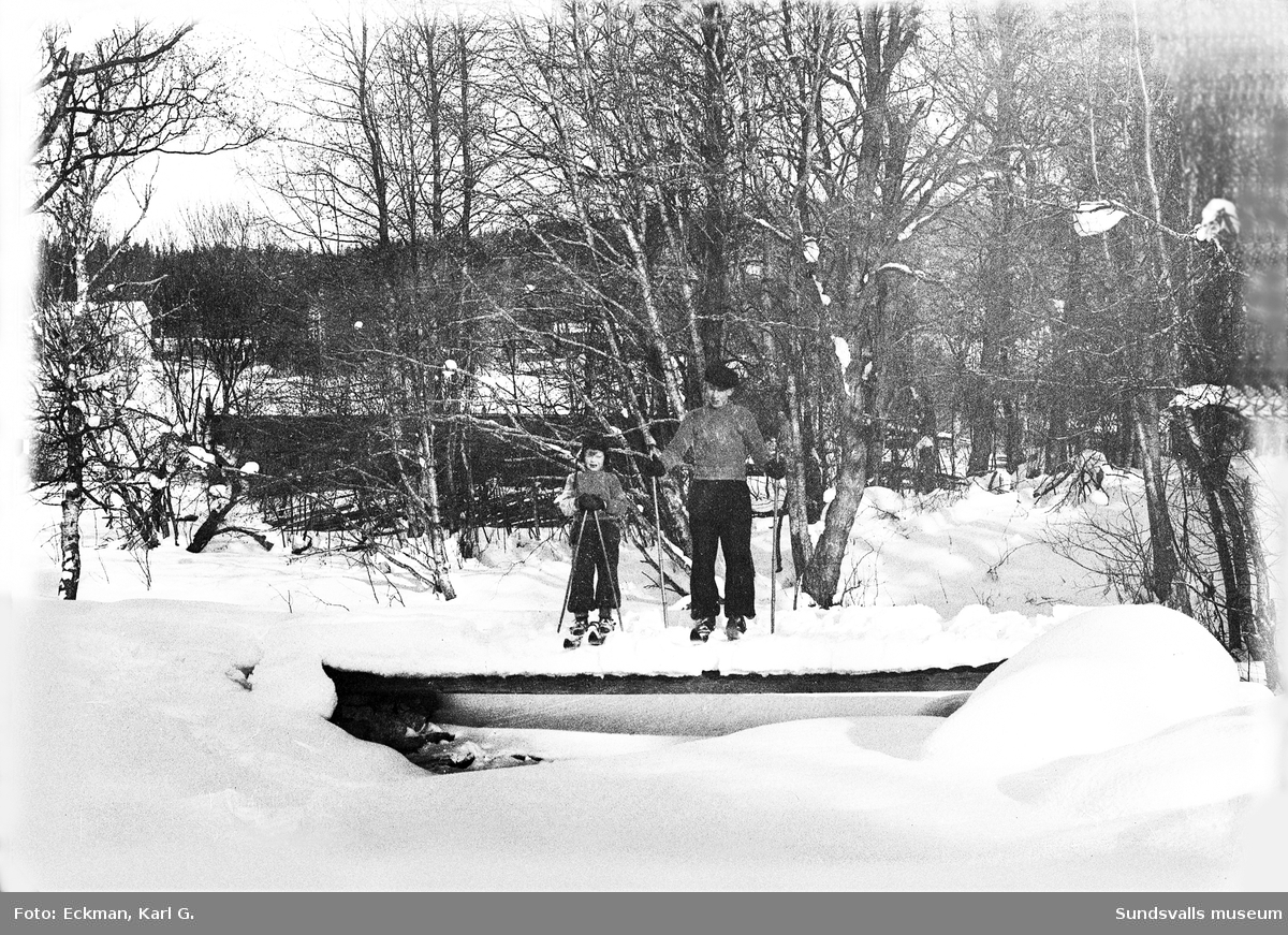 Två skidåkare poserar för fotografen på en bro över Kvarnån i Häre, Indal. Ur Karl Eckmans samling.